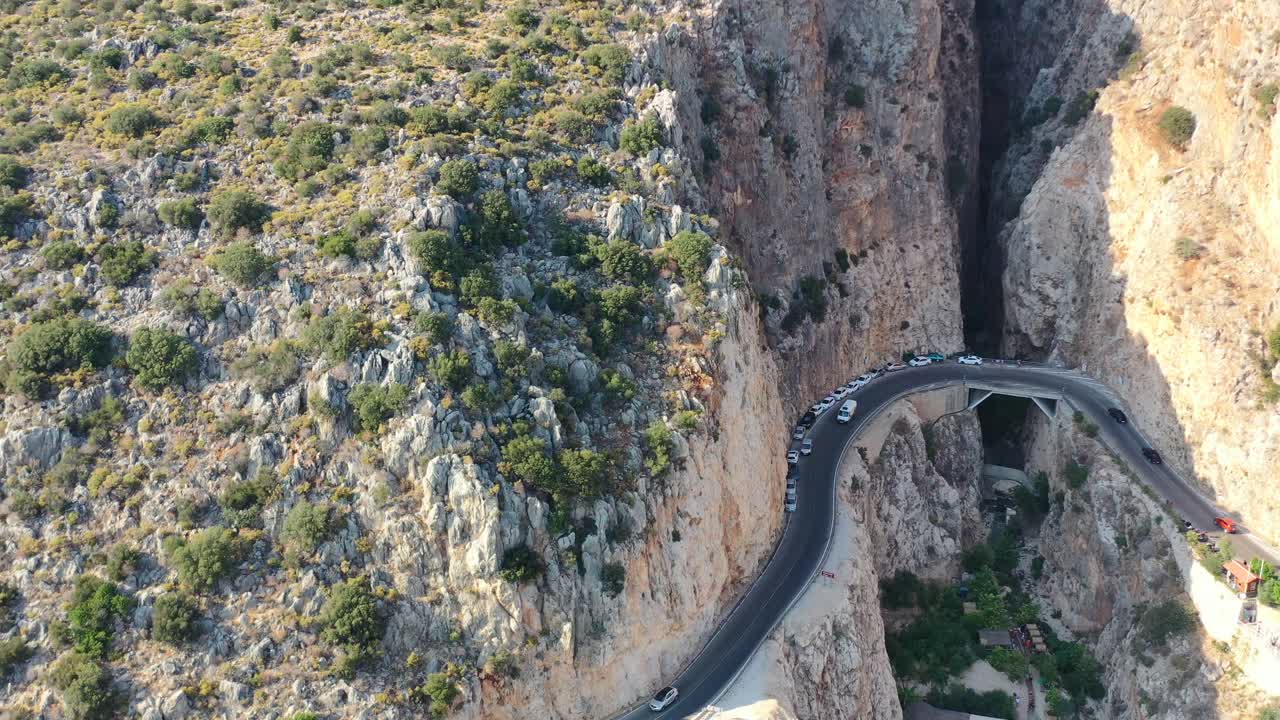 화창한 여름날 카스 터키의 카푸타스 해변에서 가파른 산 절벽을 따라 해안 도로를 따라 자동차가 이동하면서 위쪽으로 패닝하는 공중 드론