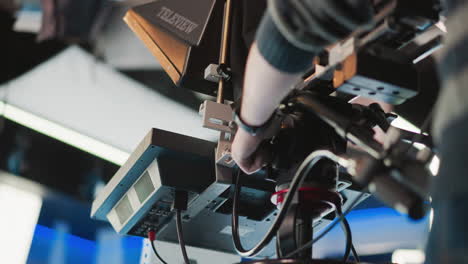 close-up of hand adjusting professional camera rig with teleprompter in broadcast studio. operator making fine adjustments to camera while controlling various settings in studio setup