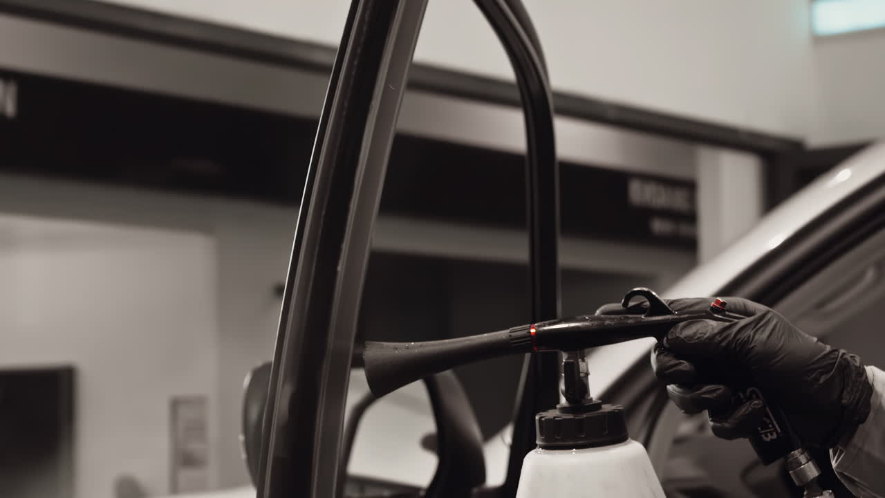 ingeniero profesional con guantes negros usando hábilmente una pistola de tornado para limpiar la ventana del coche