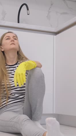 woman sitting on kitchen floor wearing rubber gloves