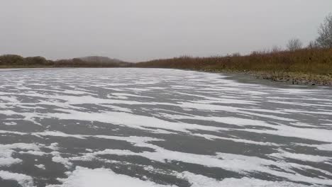 Slow-panning-shot-of-cold-blowing-snow-accumulating-along-cracks-in-ice-as-the-water-freezes