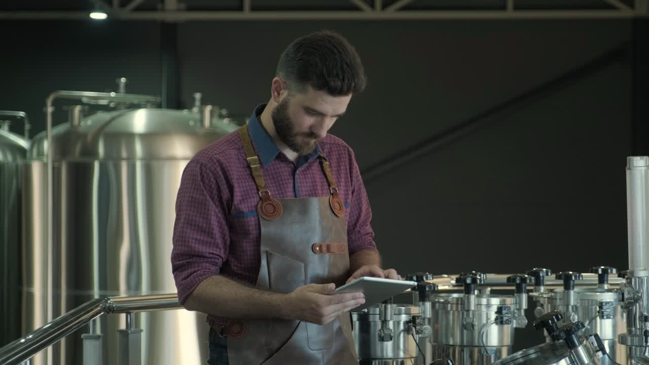 un joven cervecero con un delantal de cuero supervisa el proceso de fermentación de la cerveza en una fábrica de cerveza moderna