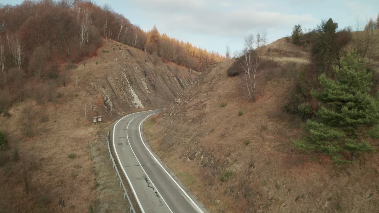 An aerial slowly descending drone view of a car driving on a winding road running through a canyon in late autumn