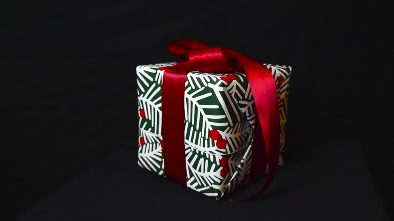 прекрасный крупный ролик рождественского подарка, упакованного в зеленую и белую оберточную бумагу и с красной лентой на темно-черном фоне студии.