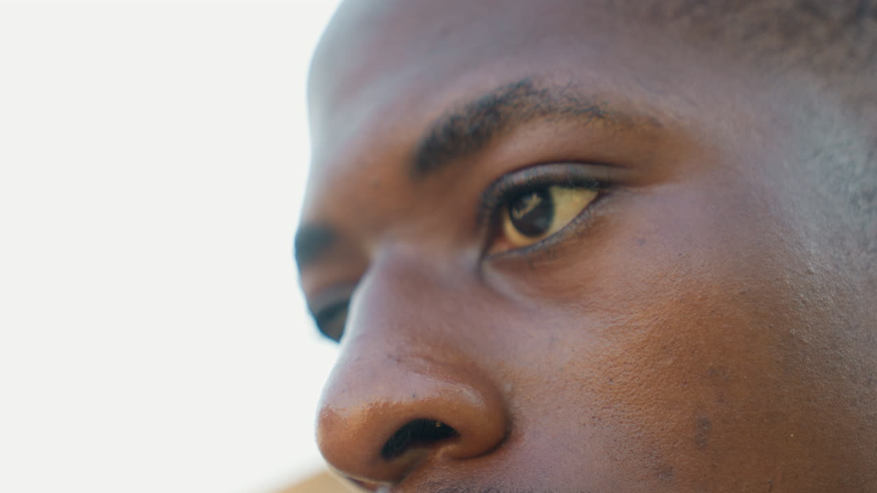 Athlete face closeup intense focused gaze, tight jaw and visible sweat, eyes tracking start line, outdoor sunlit background, portrait framing, preparation for sprint and mental focus