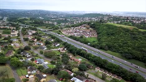 aerial footage of a drone flying over residential houses overlooking a busy highway with moving traffic in a suburb of yellow wood park durban