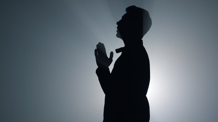 Silhouette di uomo religioso che sussurra una preghiera al chiuso. Credente che prega al buio.
