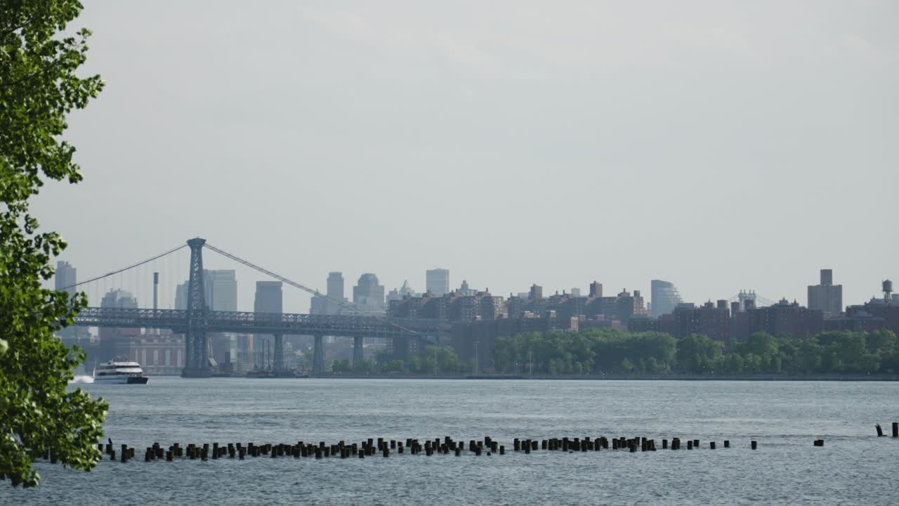 A river cruise ship catamaran powers forward, gliding past the iconic Brooklyn Bridge on New York's East River