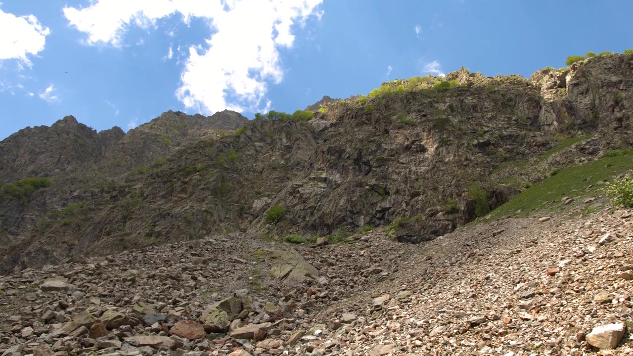 Una lenta inclinazione verso l'alto rivela un vasto campo di ghiaioni rocciosi che conduce ad aspre cime montuose.
