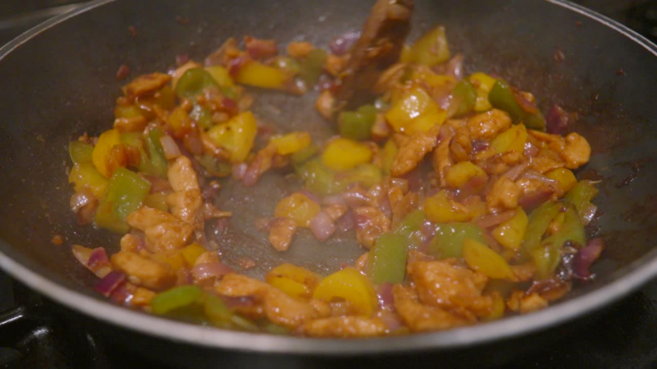 Chicken and Vegetables Cooked in Spices in Wok on High Heat with Wooden Spoon Stirring Onions, Peppers to Make Mexican Cuisine Fajitas Mix