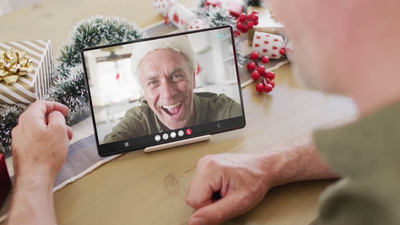 hombre caucásico con decoraciones de navidad teniendo llamada de video de tableta con hombre caucàsico feliz