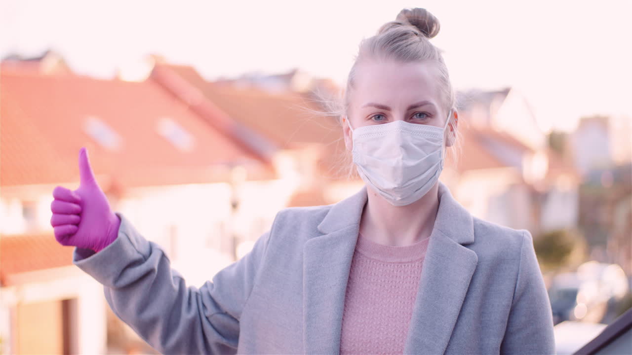 옥상에서 안면 마스크를 쓰고 엄지손가락을 치켜드는 여성의 봉쇄 샷