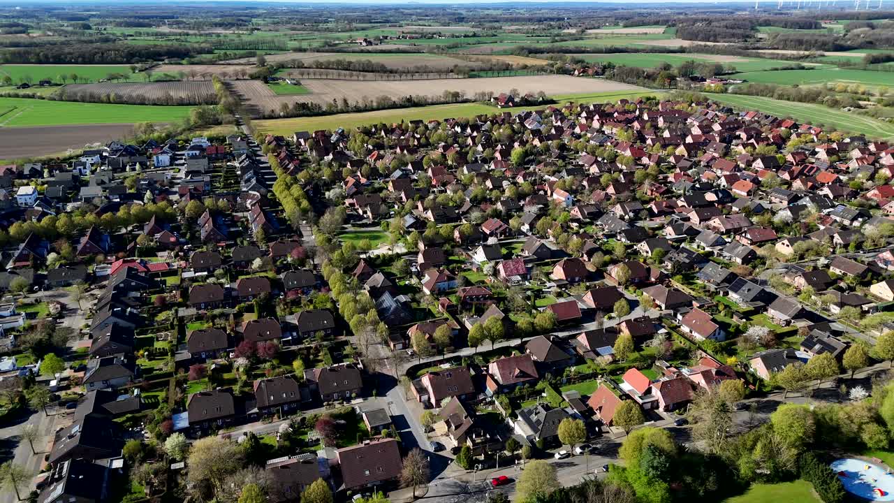 Green trees along main street with single family houses in american village town. Aerial top down flyover. Lush colored farm fields in background. Wide shot. Quiet and charming city in america.