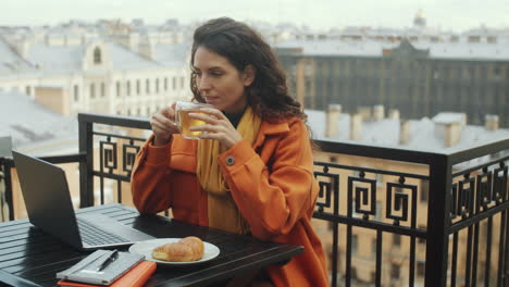 mujer de negocios usando una computadora portátil y bebiendo té en la terraza del techo