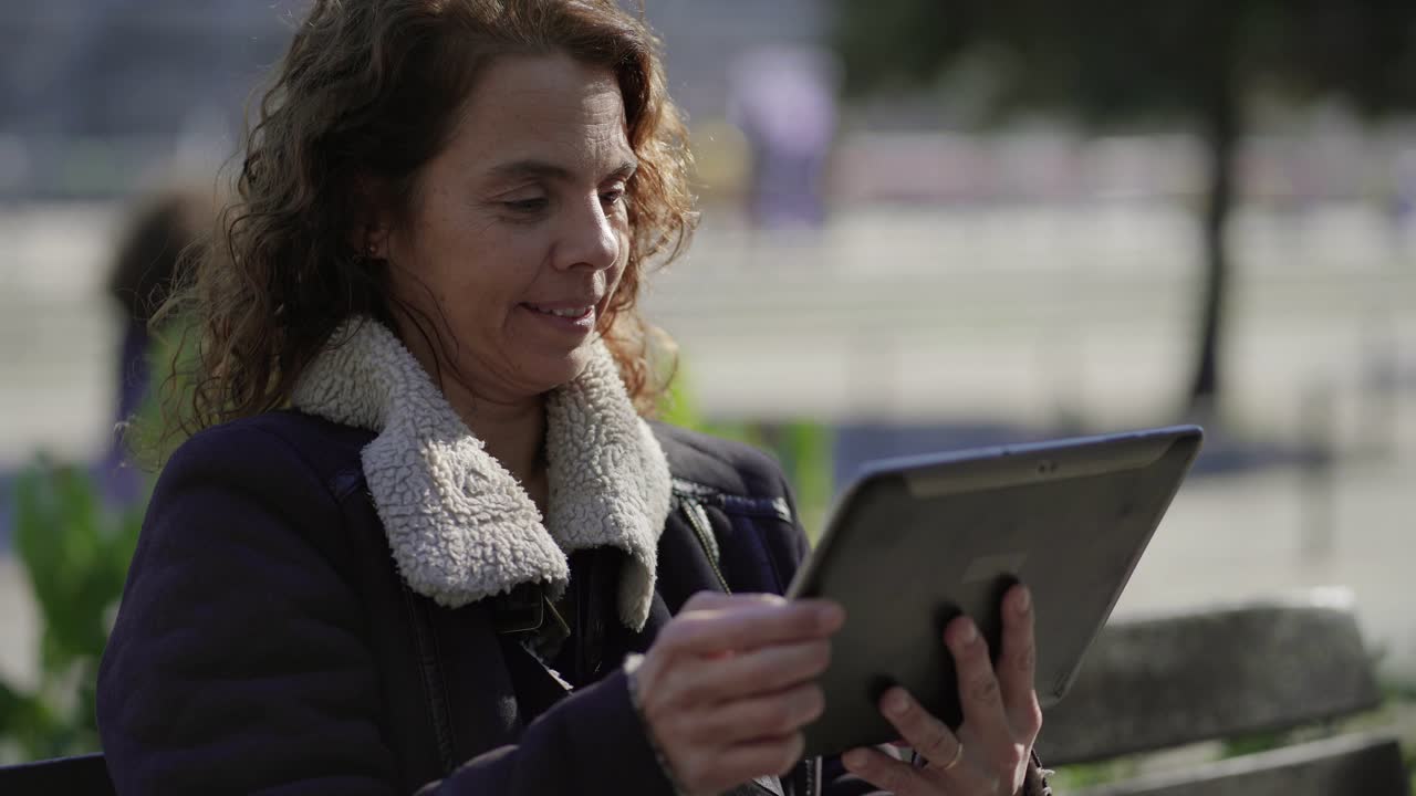 Happy mature woman wearing warm jacket using tablet outdoor
