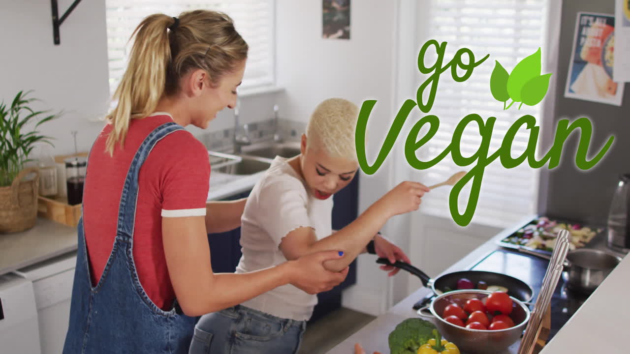 animación de texto go vegan sobre una pareja gay lesbiana bailando y cocinando juntos en casa
