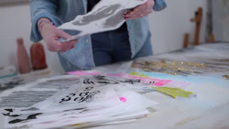 female artist selecting swashes for canvas, stood in a home studio, surrounded by her paintings