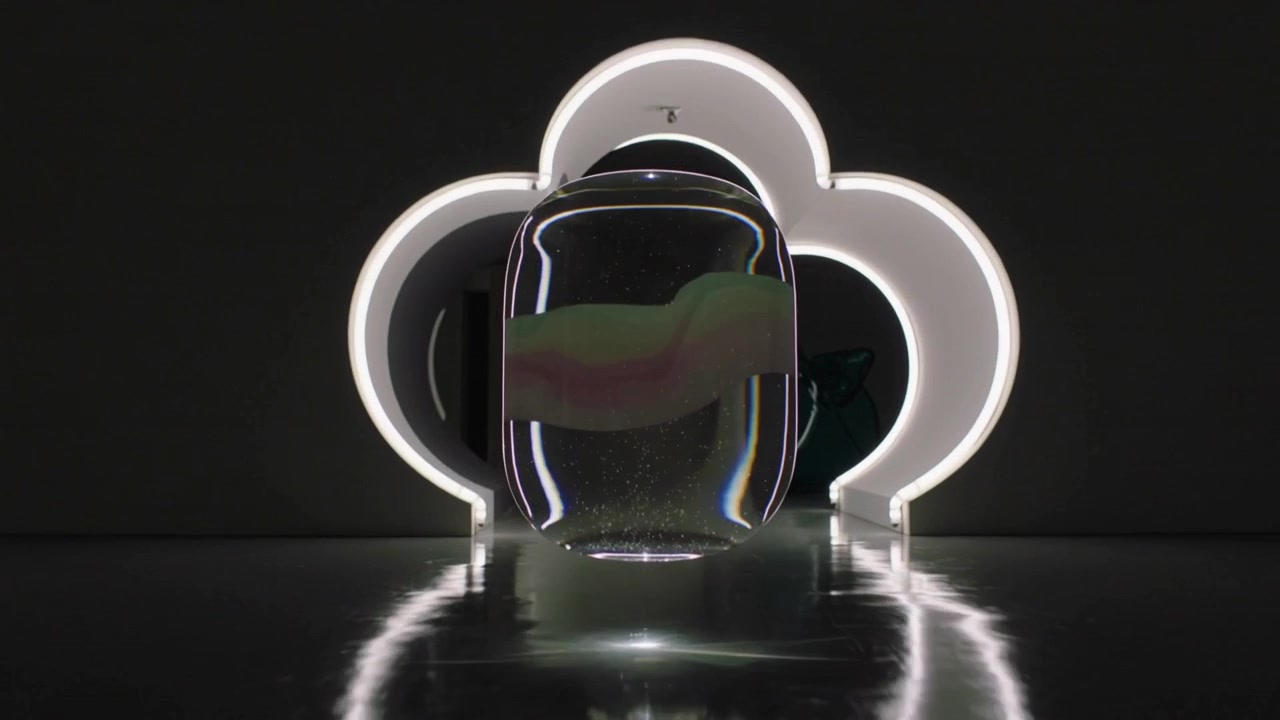 La telecamera si allontana, una capsula levita sopra il pavimento in uno studio, mostrando un arco illuminato e vetro verde.
