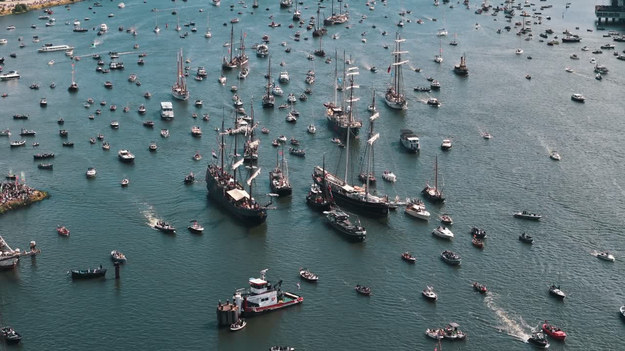 Aerial shot rising and panning up to reveal the city of Amsterdam beyond the tall ships