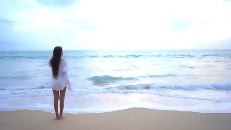 Mujer-De-Pie-Descalza-Frente-Al-Mar-Al-Atardecer-Cuando-El-Agua-De-Mar-Espumosa-Rueda-Hacia-La-Playa-De-Arena,-Plantilla-De-Vacaciones