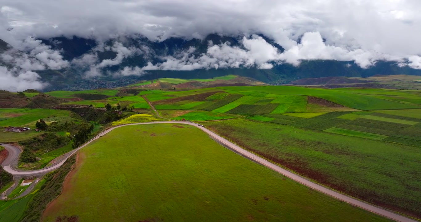 Campi agricoli di un verde vibrante e strada rurale sotto nuvole drammatiche nel distretto di Maras della Valle Sacra, Perù. Drone aereo.