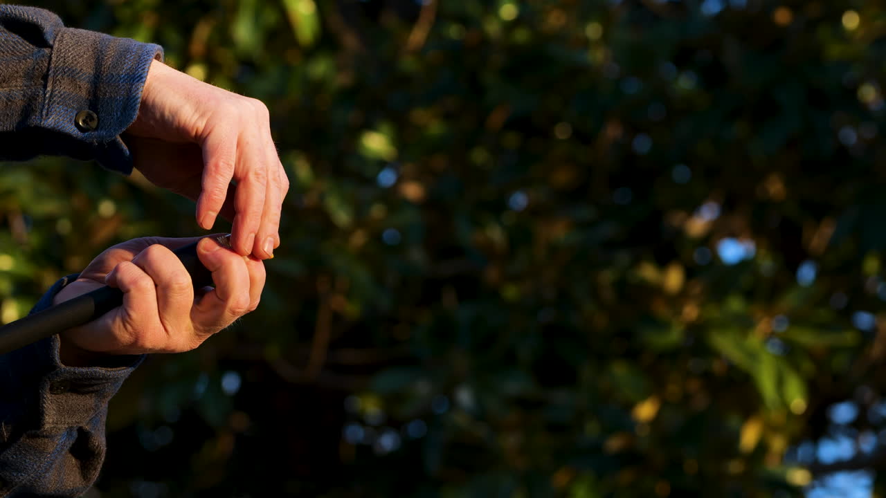 Male caucasian hands attach yellow nozzle to power washer with trees in the background