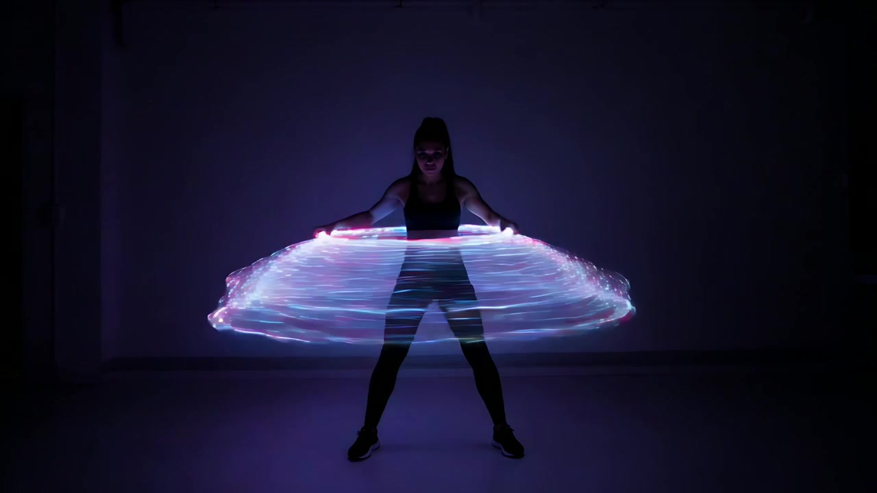 LED che si accendono, ballerina che fa girare un cerchio LED in vita in uno studio buio, esibendosi in abbigliamento sportivo.