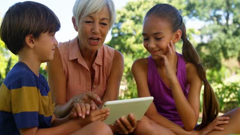 abuela y nietos usando tableta digital en el parque 4k