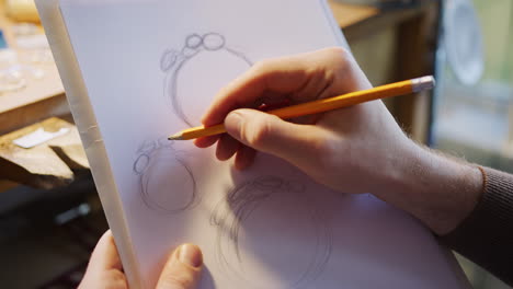 close up of male jeweller sketching out design for ring in studio