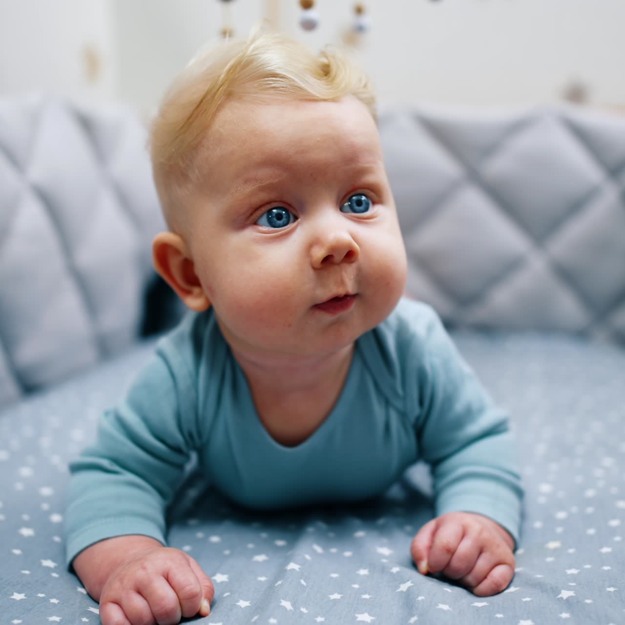 Nydelig blåøyd blond baby ligger i vuggen. Søt, rolig spedbarnsgutt ser overrasket rundt. Nærbilde.