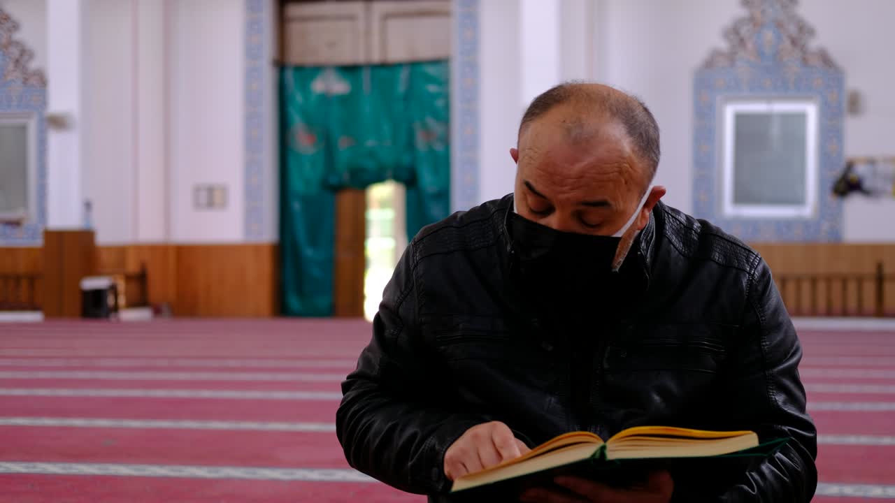 마스크를 쓴 성인 남자가 코란 모스크를 읽습니다.