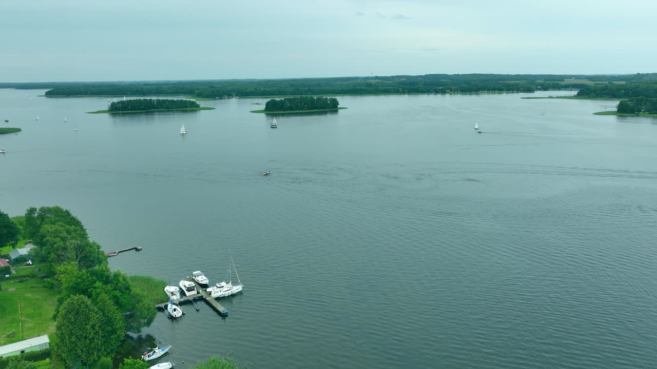 Aerial view of Jeziorak lake with small docks and boats moored by the shore, surrounded by lush greenery and small islands in the distance, ideal for summer recreation