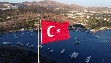 fotografía aérea estática de la bandera de turquía revoloteando en el viento, la costa de gumusluk en el fondo