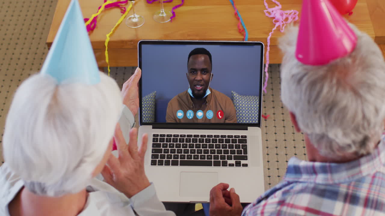 Caucasian senior couple on laptop video chat wearing party hats at home
