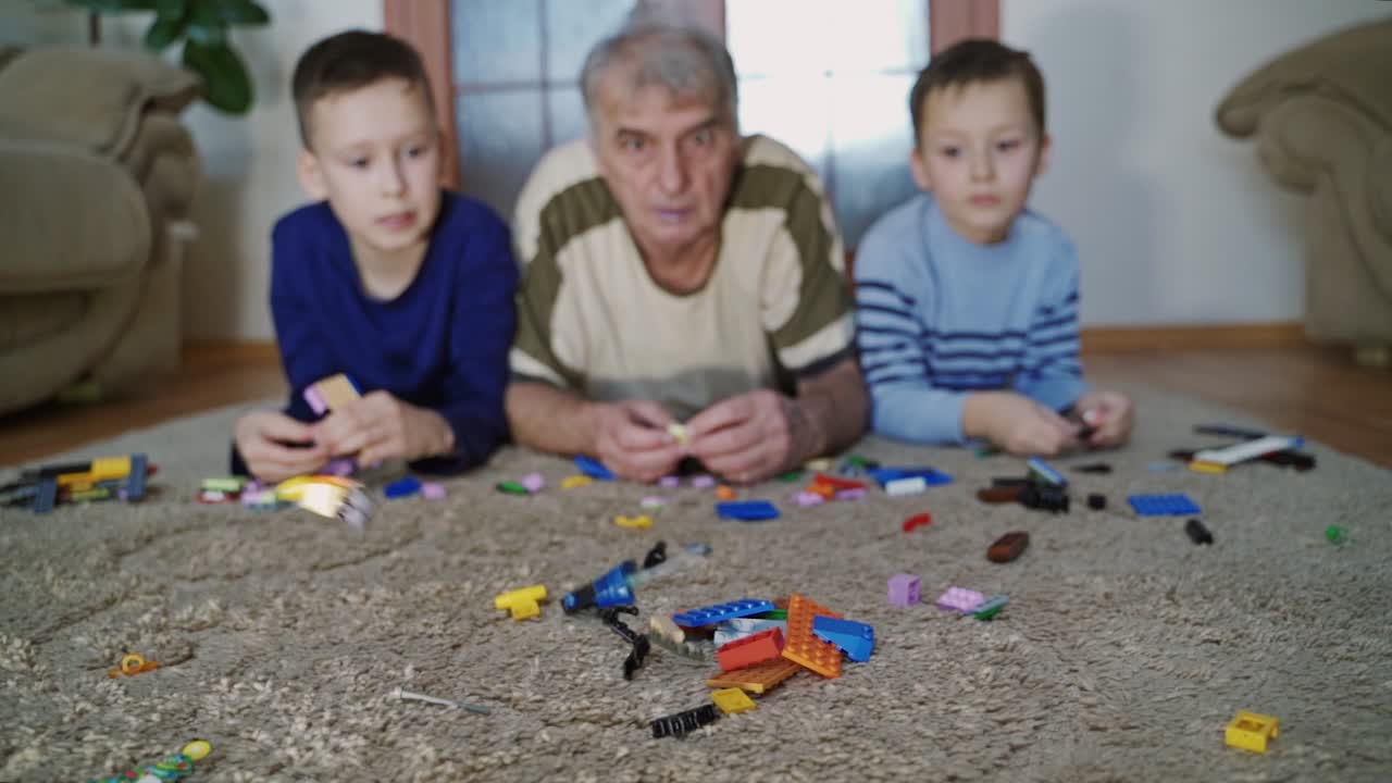 Nonno e nipoti giocano nella stanza. Piccoli ragazzi felici che giocano con il nonno con blocchi di plastica colorati.
