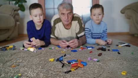 grandfather and grandsons play in the room. little happy boys playing with grandfather with colorful plastic blocks