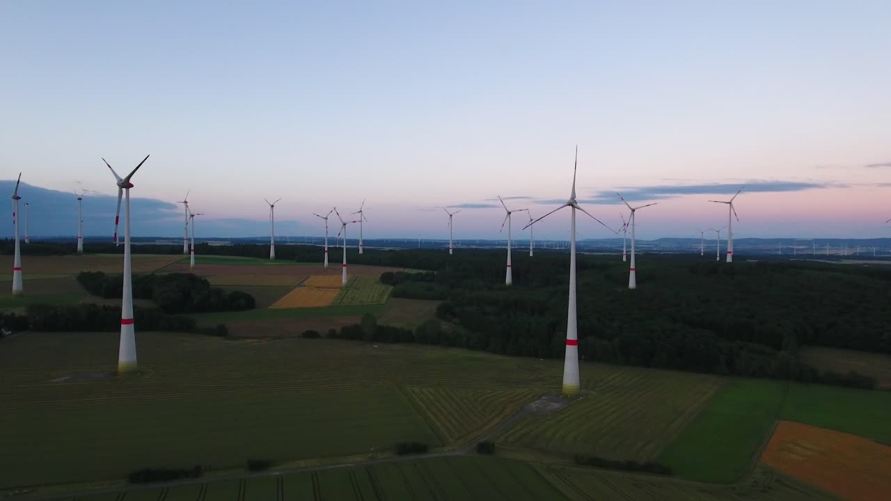 Drone aerial flying towards wind turbine farm in a large open field