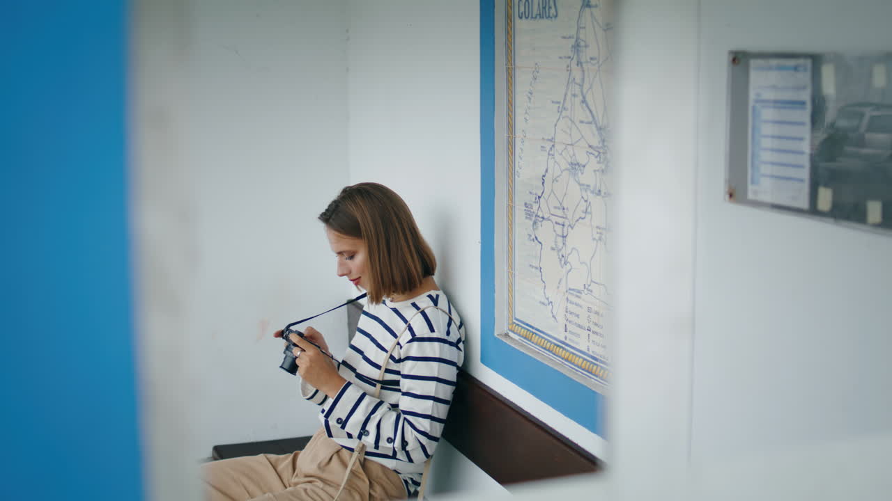 Girl sitting bus stop in old european town vertically shot. Tourist hold camera
