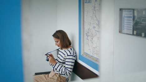 Girl-sitting-bus-stop-in-old-european-town-vertically-shot.-Tourist-hold-camera