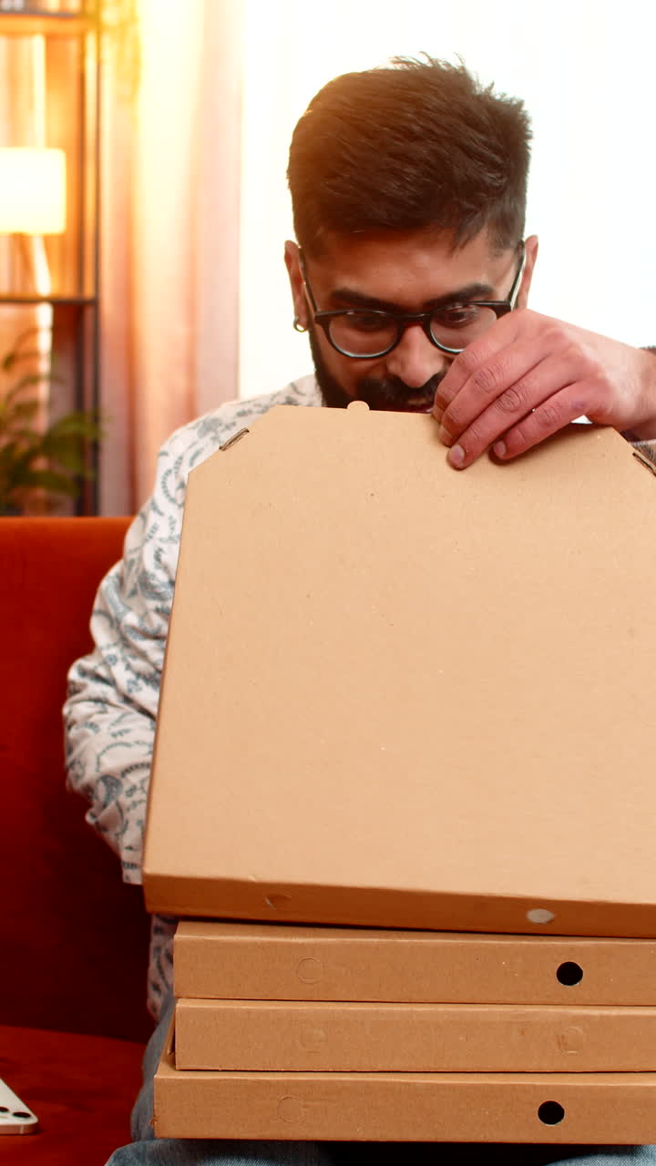 Indian man ordering fast food online with smartphone and card happily receiving pizza boxes delivery