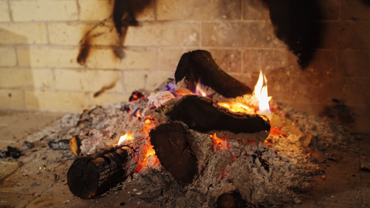 Cozy fireplace. Smoldering logs in ash. Embers of burnt-out fire in fireplace at home. Background of burning wood in slight flame. Close-up.
