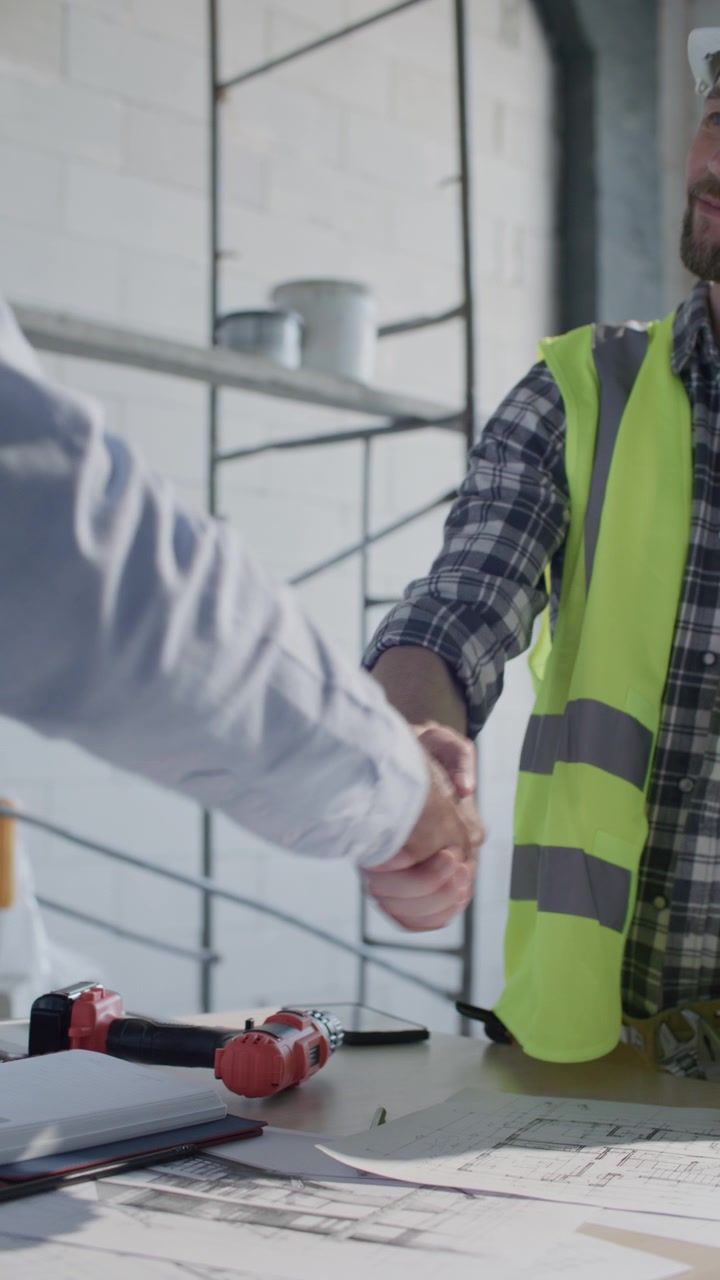 Obrero de construcción y Jefe de obra estrechando manos sobre planos de planta