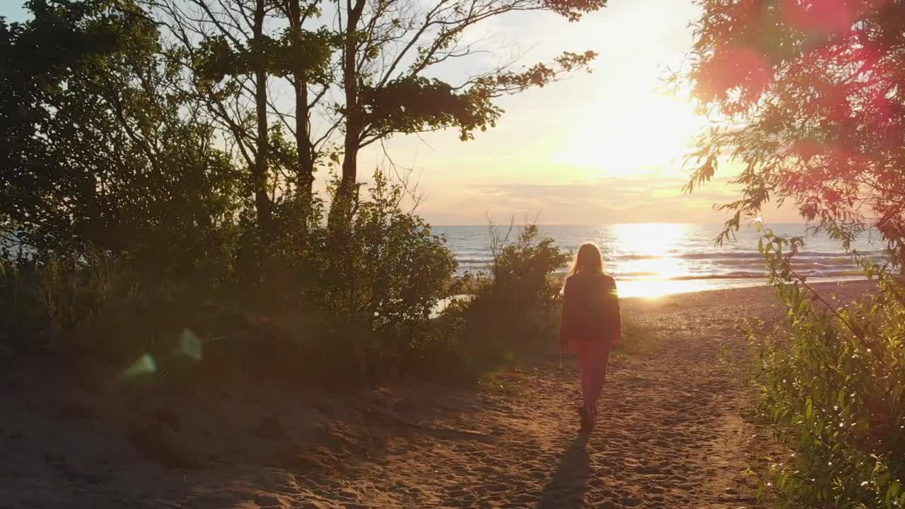 mujer caminando hacia la puesta de sol sobre el mar báltico, vista de seguimiento posterior