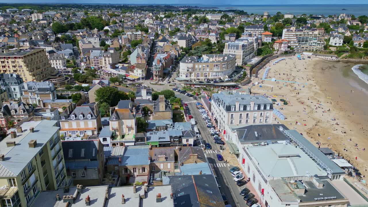 Aerial of Plage de l’Ecluse in Dinard with beachgoers, turquoise water, and promenade, summer establishing