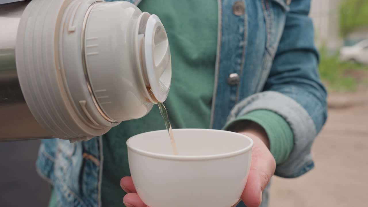 Caucasian Woman Pouring Coffee Into Cup Outdoors Steady Stream From Thermos Into Paper Cup Denim Sleeves Rolled Hands Steady Urban Parking Backdrop Gesture Of Sharing Warm Hospitality Focused Liquid