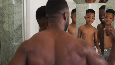 african american father and son flexing their muscles in mirror together