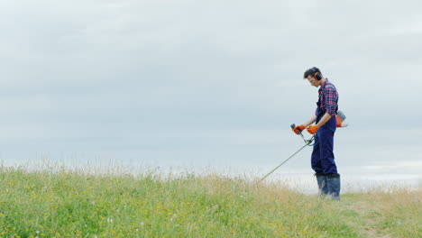 Young-Man-Mowing-Grass-With-A-Trimmer-On-A-Picturesque-Meadow