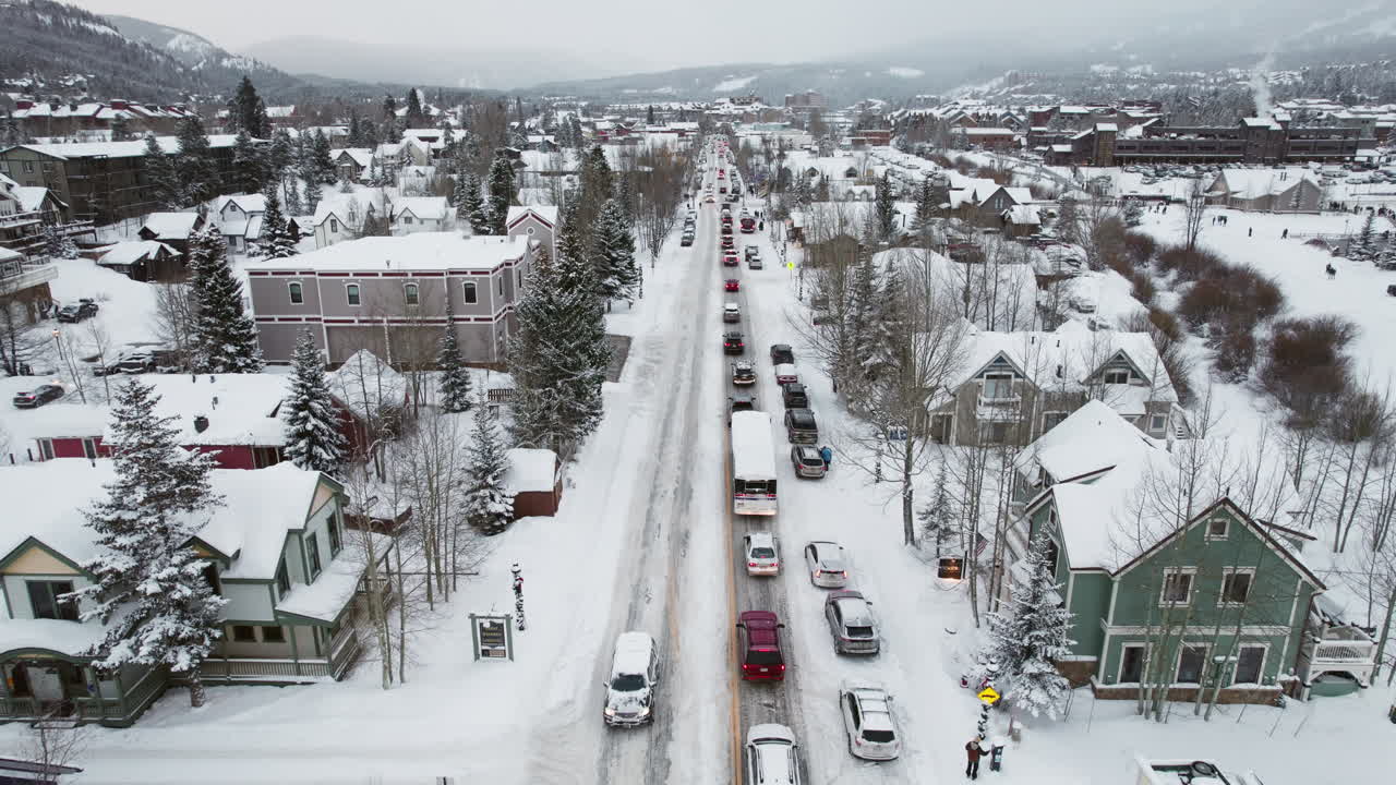 An aerial of a peaceful and beautiful snow-covered Breckenridge, as cars drive through snow on the main road through the popular Colorado mountain town for a ski vacation at the world famous resort.