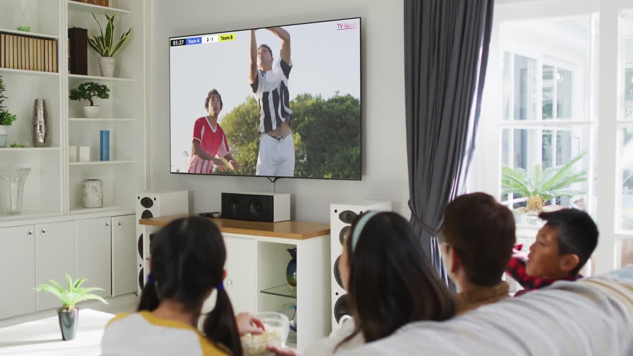 아들과 딸이 소파에 앉아서 집에서 축구를 보는 아시아 커플의 비디오