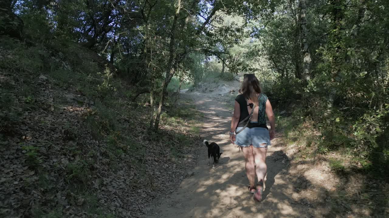 una mujer y su perro caminando por un sendero entre árboles y follaje
